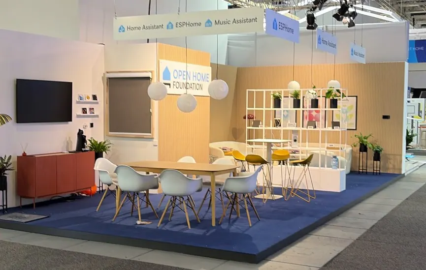 The Open Home Foundation’s IFA Berlin booth, furnished with a sofa, tables, chairs and shelving beneath Home Assistant, ESPHome and Music Assistant signs.